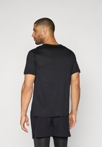 Black short-sleeve t-shirt with a textured pattern, crew neck design, smooth fabric, and a relaxed fit, worn by a person seen from the back.