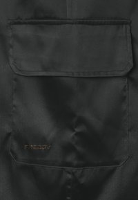 Tessuto nero con una superficie liscia, caratterizzato da una tasca a toppa. Un logo con la scritta "FREDDY" è impresso in oro nell'angolo in basso a destra.