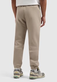 Beige sweatpants met een elastische tailleband en boorden, met een gladde, zachte textuur. Gedragen met lichtgrijze en gele sneakers.