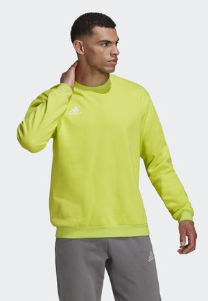 Neon-gelbe Sweatshirt mit langen Ärmeln, Rundhalsausschnitt, glatter Textur und einem weißen Adidas-Logo auf der linken Brust. Kombiniert mit grauen Hosen.
