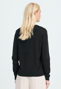 Pullover nero a maglia con maniche lunghe, scollo rotondo e polsini e orlo a costine. Texture morbida con un design classico e semplice.