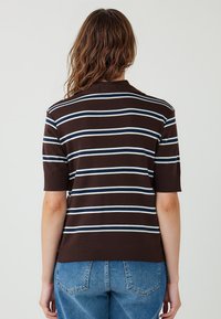 Bruine gestreepte korte mouwen top met verticale blauwe en witte strepen, geribbelde kraag en een getailleerd ontwerp, gecombineerd met lichtblauwe jeans.