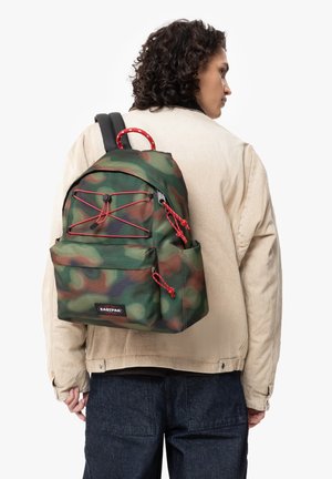 Green camouflage backpack with red accents, featuring a front pocket, two adjustable straps, and a drawstring closure. Brand label visible.