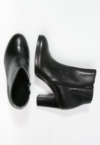 Une paire de bottes noires en cuir à talons blocs et fermetures éclairs latérales, présentée en vue de dessus et de côté sur un fond blanc.