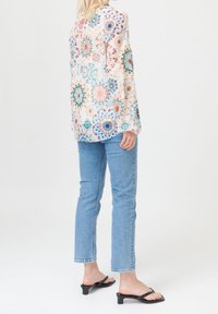 Blouse à manches longues et transparente avec un motif floral aux couleurs pastel. Associée à un jean droit bleu clair et des sandales noires minimalistes.