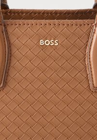 Rjava tkana usnjena torbica z teksturirano površino, na sprednji strani pa izstopa zlata nalepka z napisom "BOSS".