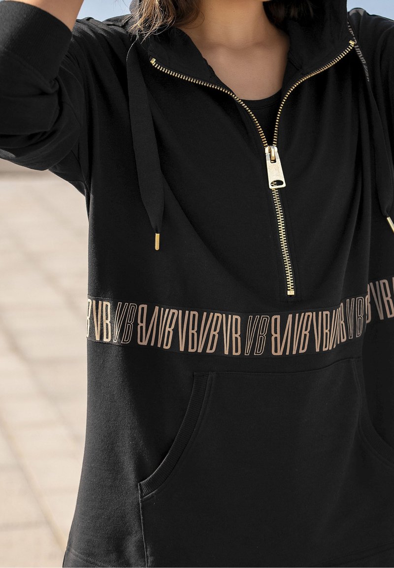 Sweat à capuche noir avec demi-fermeture éclair et cordons, avec une bande de texte beige répétée "BVB" sur la poitrine et des poches à l’avant.