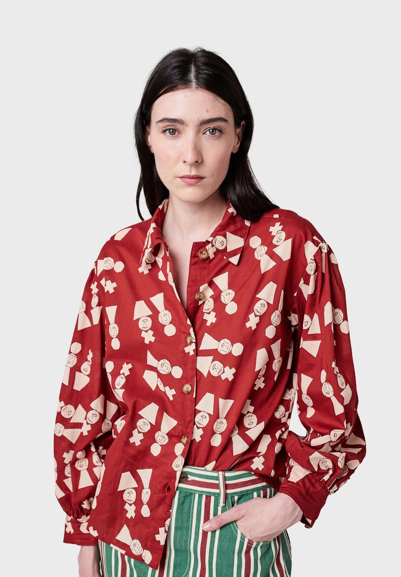 Camicia in cotone rosso con vestibilità oversize, con fantasie bianche giocose di figure e forme, dotata di chiusura con bottoni sul davanti e maniche lunghe.