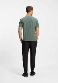 T-shirt verde a maniche corte abbinato a joggers neri slim, con polsini elastici e scarpe sportive nere. Tessuto morbido, vestibilità casual.
