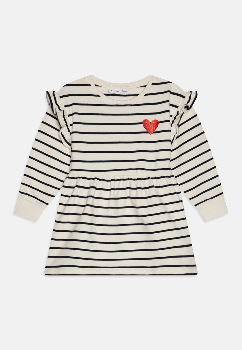 Dryžuota suknelė su ilgomis rankovėmis, kreminė bazė, tamsiai mėlynos juostos, plonyti pečių akcentai ir raudona blizgučių širdis ant krūtinės.