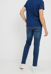 Marinblå kortärmad skjorta med prickigt mönster, parat med slim fit blå jeans och vita sneakers. Bakifrån visas detalj på baksidan av båda plaggen.