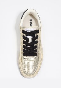Zapatilla con un upper texturizado de oro brillante, cordones negros y un forro blanco. Presenta una tapa de talón negra y una etiqueta que dice "BIMBA."
