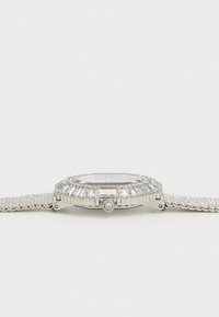 Ceas din oțel inoxidabil cu un cadran dreptunghiular, cu bezel ornamentat și accente asemănătoare cu diamante. Dispune de o curea din plasă și o finisare lustruită.