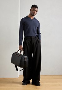 Suéter azul marino con cuello, acompañado de pantalones de pierna ancha negros. Bolso de viaje de cuero negro con detalles en cuero marrón.
