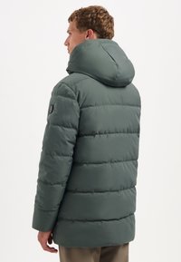 Groene pufferjack met capuchon, voorzien van een gewatteerd ontwerp, een gladde textuur en een logo-opdruk aan de zijkant. De pasvorm is relaxed.