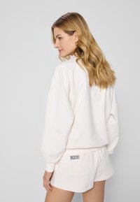 Lichtroze oversized sweatshirt en bijpassende shorts. Zachte stof met geribbelde manchetten. "BIZUU" logo detail op de achterzak van de shorts.