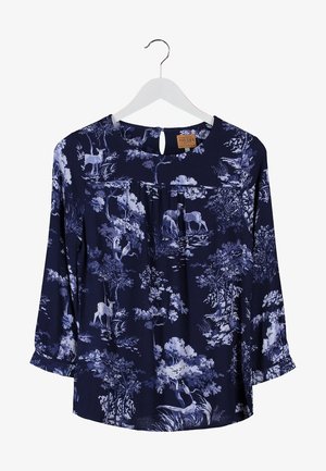 Granatowa bluzka w kwiaty z rękawami do trzech czwartej, w połączeniu z ciemnymi obcisłymi dżinsami i czarną kopertówką. Posiada skomplikowane wzory kwiatowe.