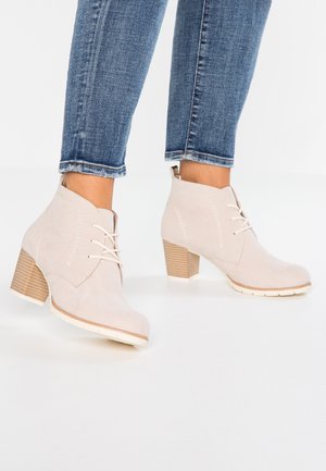 Botas de tobillo de ante beige con punta redonda, diseño de cordones y tacón de madera apilada. Parte superior texturizada con acentos de costura.