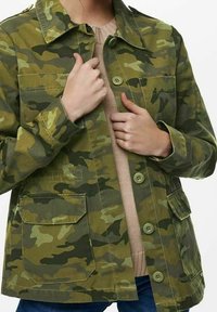 Camouflagejakke i grønne nuancer med knaplukning fortil, to klaplommer og en klassisk krave. Fremstillet af et robust, tekstureret stof.