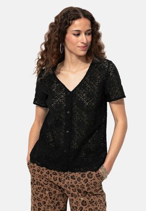 Blouse noire en dentelle à manches courtes avec un col en V, dotée d'une fermeture à boutons et d'un design à motifs détaillés. Assortie à un pantalon imprimé léopard marron.