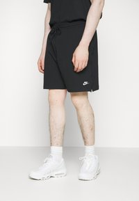 Black athletic shorts with a drawstring waist and side pockets, featuring a white Nike logo on the lower left. Worn with white sneakers.