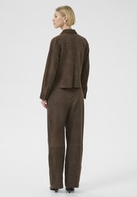 Bruine leren jas met bijpassende wijde broek, met een gladde textuur en een op maat gemaakte pasvorm, gezien vanuit de rug.