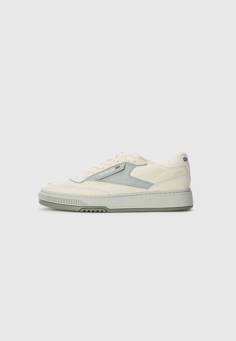 White and grey sneakers with a leather upper, a textured design, flat laces, and a rubber sole. Features a logo on the side and back.