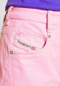 Rosa denimshorts med en distinkt bakficka som visar en märkesskylten. Har guldhardware och texturerad tyg.