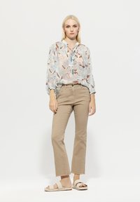 Leichtes Blumenblusenoberteil mit Bindekragen, beigefarbene High-Waist-Hosen mit fransigen Säumen und beigefarbene gewebte Rutschen-Sandalen. Weiche Texturen, Pastellfarben.