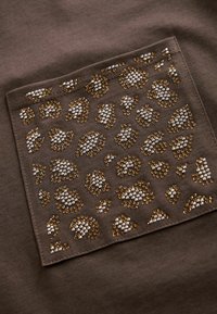 Tissu marron avec une poche texturée présentant un motif léopard souligné de rhinestones dorés et argentés, ajoutant de l'éclat à la surface.