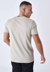 Camiseta de manga corta color beige claro con un diseño de gofre texturizado, cuello redondo y un corte relajado, vista desde la parte trasera.