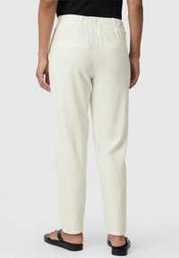 Crème-kleurige broek met een zachte, gladde textuur, voorzien van een relaxte pasvorm, achterzakken en een comfortabele tailleband. Draag het met zwarte sandalen.