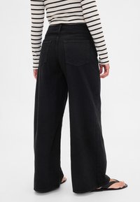 Svarta vida denimbyxor med hög midja, två bakfickor och en ledig passform, kombinerade med en randig svartvit långärmad tröja.