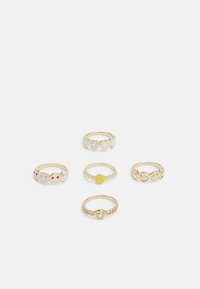 Cinco anéis em metal dourado; os designs incluem corações e rostos sorridentes, com detalhes coloridos em vermelho e amarelo e texturas variadas.