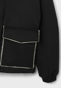Schwarze Jacke mit einer großen, asymmetrischen Tasche, die mit einem Kunstfellfutter versehen ist. Sie hat elastische Bündchen und kontrastierende weiße Nähte.
