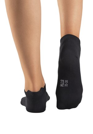 Schwarze Knöchelsocken, die auf nackten Füßen präsentiert werden, mit einem gewellten oberen Rand und einer Größenangabe, die auf der Ferse aufgedruckt ist. Weicher Stoff, elastisches Material.