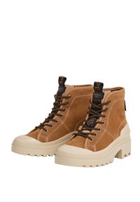 Bruine suède hoge laarzen met een dikkige beige zool en zwarte veters, met een merklabel aan de achterkant van de enkel.