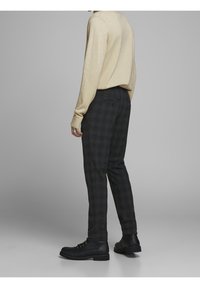 Cremefarbener Strickpullover kombiniert mit dunkelkarierter Hose und schwarzen Schnürstiefeln. Das Outfit zeichnet sich durch eine lockere Passform und strukturierte Stoffe aus.