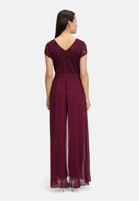 Bordeauxfarbenes Kleid mit einem Spitzen-Oberteil, kurzen Ärmeln und einem V-Ausschnitt auf der Rückseite. Der Rock hat transparente Lagen und ein plissiertes Design.