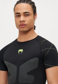 Camisa deportiva negra de manga corta, con un diseño texturizado, logo de serpiente verde y líneas de acento verde claro en curva.