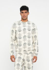 Sudadera blanca con un patrón floral y de hojas en gris, puños acanalados y cuello redondo, combinada con pantalones a juego con el mismo patrón.
