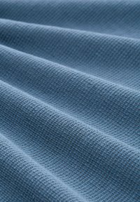 Blauer strukturierter Stoff mit einem gewebten Muster, in sanften Falten präsentiert, das seine glatte Oberfläche und die einheitliche Farbe überall zeigt.