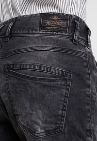 Svarta denimjeans med smal passform, med bakfickor och sömdetaljer. Midjebandet har en brun läderetikett med varumärkeslogotyp.