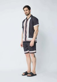 Chemise à manches courtes bleu marine avec des rayures rose clair et blanches, associée à un short assorti avec des accents rayés et des sandales noires à glissière.