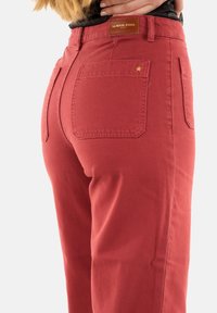 Pantaloni in cotone rossi con una vestibilità strutturata, dotati di una tasca posteriore con un piccolo dettaglio a forma di stella e un'etichetta in pelle con marchio sulla cintura.