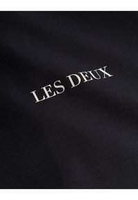 Black fabric with a smooth texture featuring the white text "LES DEUX" prominently displayed in a classic font.