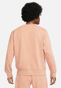 Světle růžový svetr s kulatým výstřihem a dlouhými rukávy, vyrobený z texturované látky s žebrovanými manžetami a lemem.