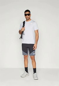 Λευκό κοντομάνικο μπλουζάκι, σορτς με μαύρο και γκρι σχέδιο, μαύρες κάλτσες και γκρι παπούτσια. Αξεσουάρ περιλαμβάνουν γυαλιά ηλίου και σακίδιο.