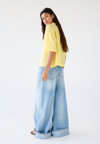 Gele korte mouwen shirt gecombineerd met oversized lichtblauwe denim jeans. De jeans hebben grote omslagen en een klassieke vijf-pocket stijl.