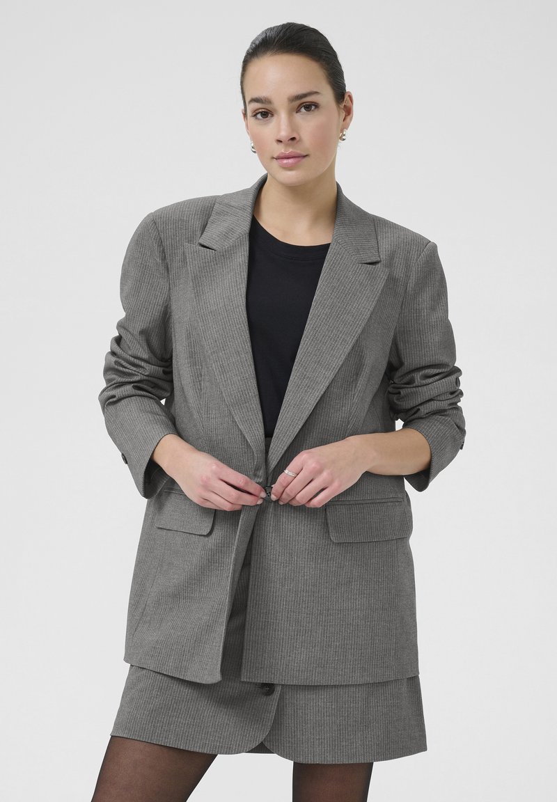 Grijze blazer met streepdessin en een relaxed fit, met enkele knoopsluiting en twee voorzakken, gecombineerd met een zwarte top en bijpassende rok.